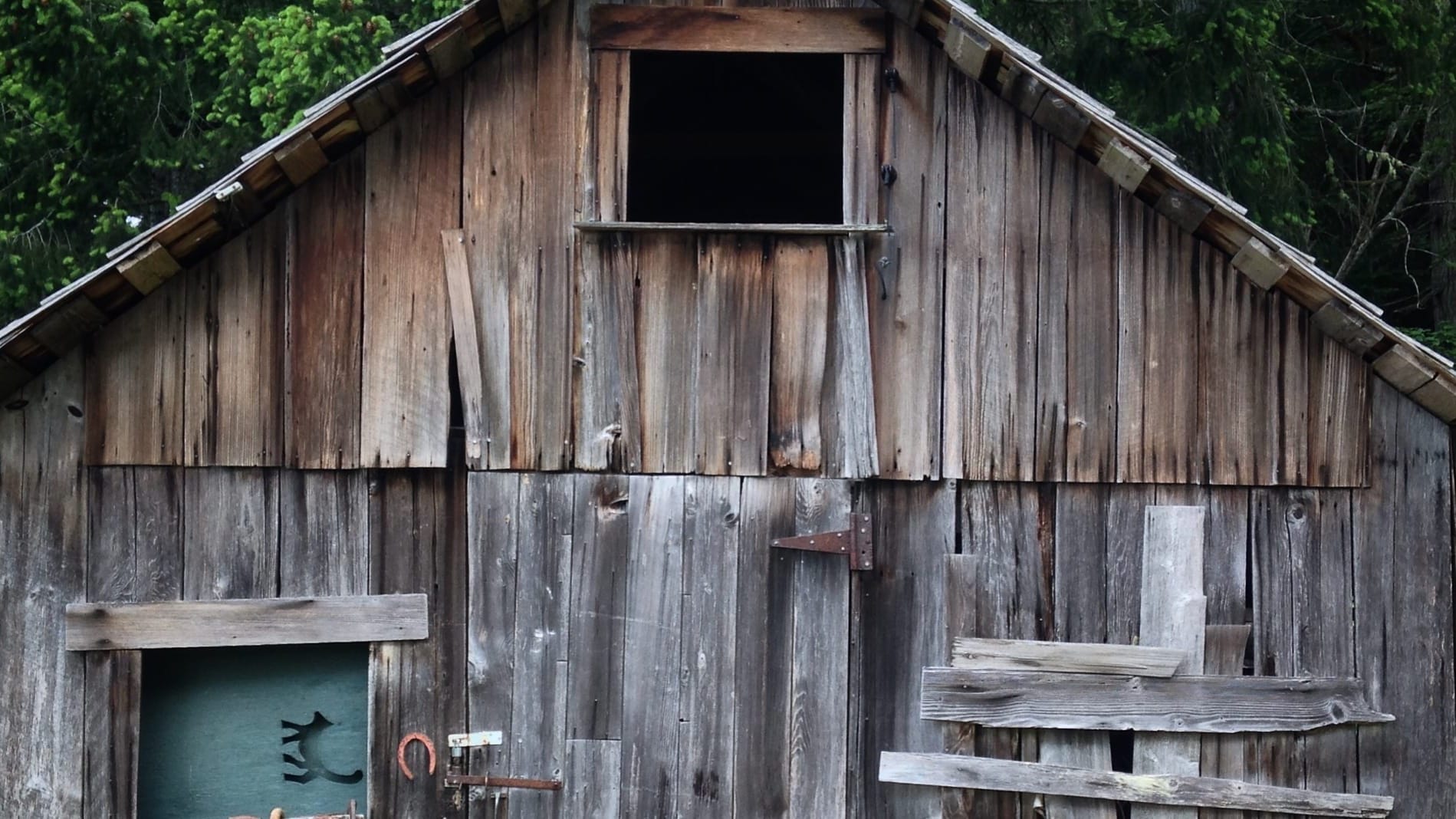 A weirdly cropped close-up of the front of a fairly dilapidated old barn in a clearing, trees visible behind.