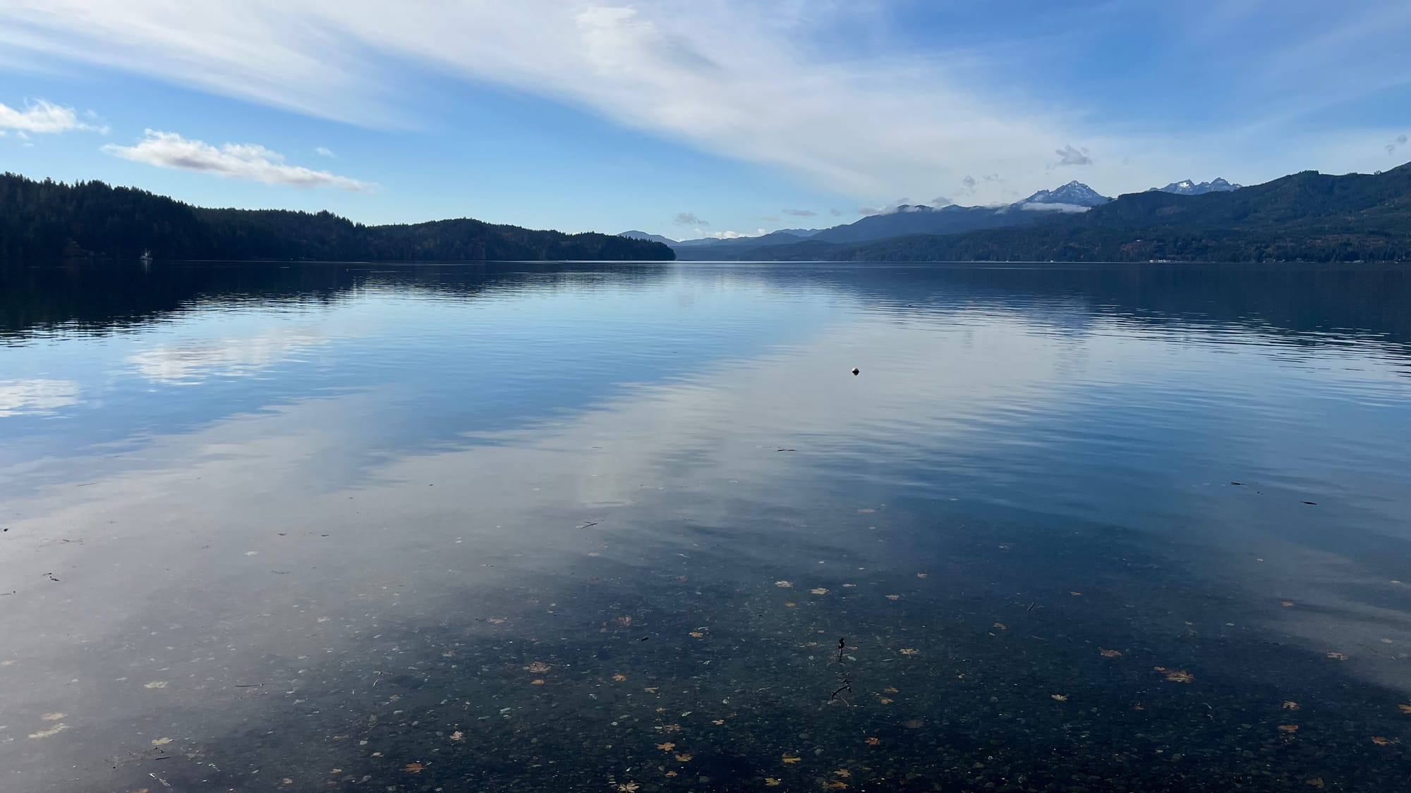 A somewhat cloudy, very cool day. Clouds are reflected in a body of water. In the distance: mountains.